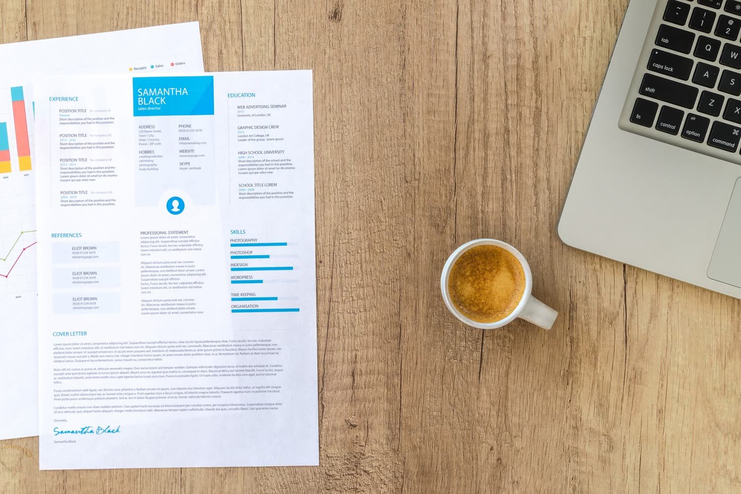 Un CV imprimé posé sur un bureau à côté d’un ordinateur portable et d’un café