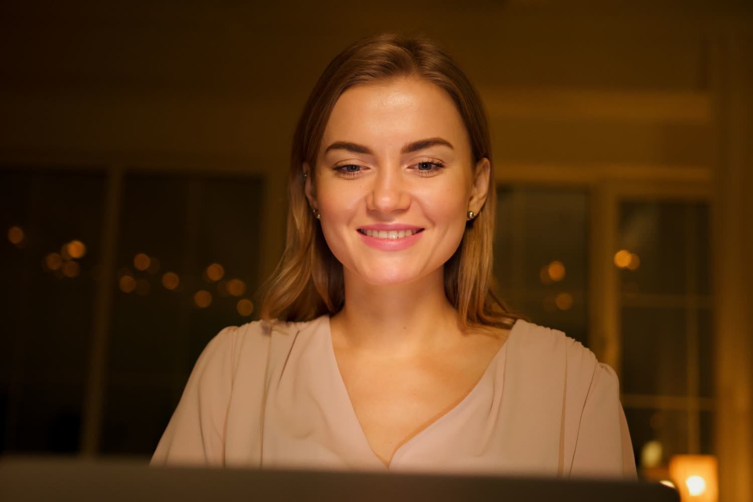 Une femme souriante devant son ordinateur le soir, détendue pendant que son système travaille